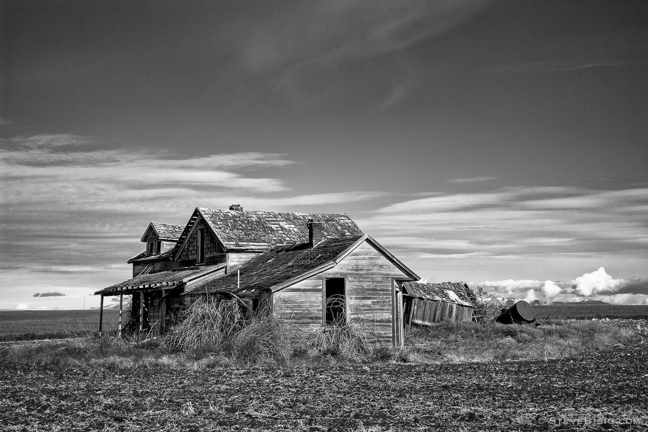 A black and white photograph of an old abandoned farm house in rural Withrow, Washington.