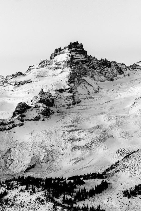 A black and white photograph of the rising sun shining on Little Tahoma (Mt. Rainier) as viewed from Sunrise, Mount Rainier National Park, Washington