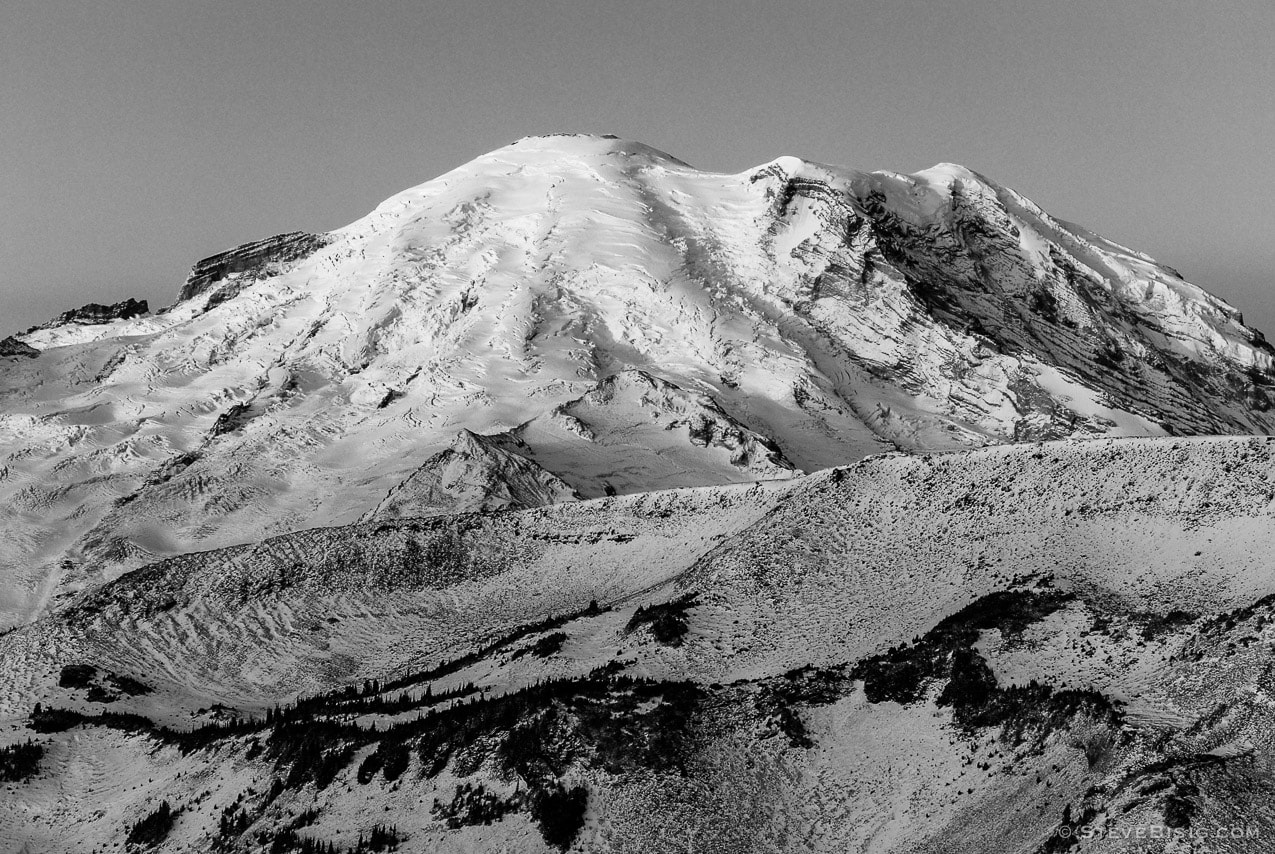 A black and white photograph of the rising sun shining on Mount Rainier as viewed from the Sunrise area of Mount Rainier National Park, Washington.