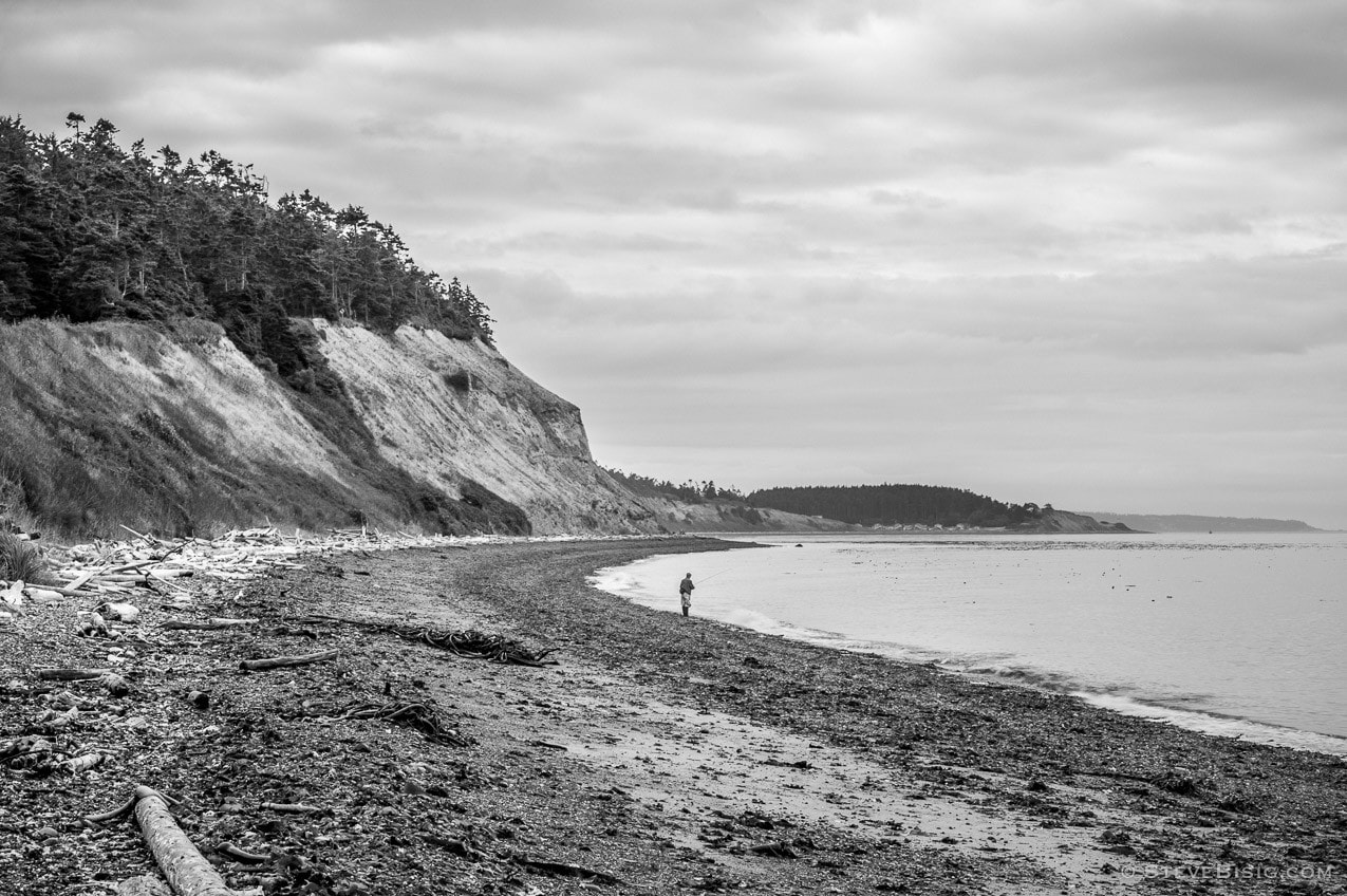 A black and white photograph of a fisherman along the Puget Sound at Ebey's Landing on Whidbey island near Coupeville, Washington.