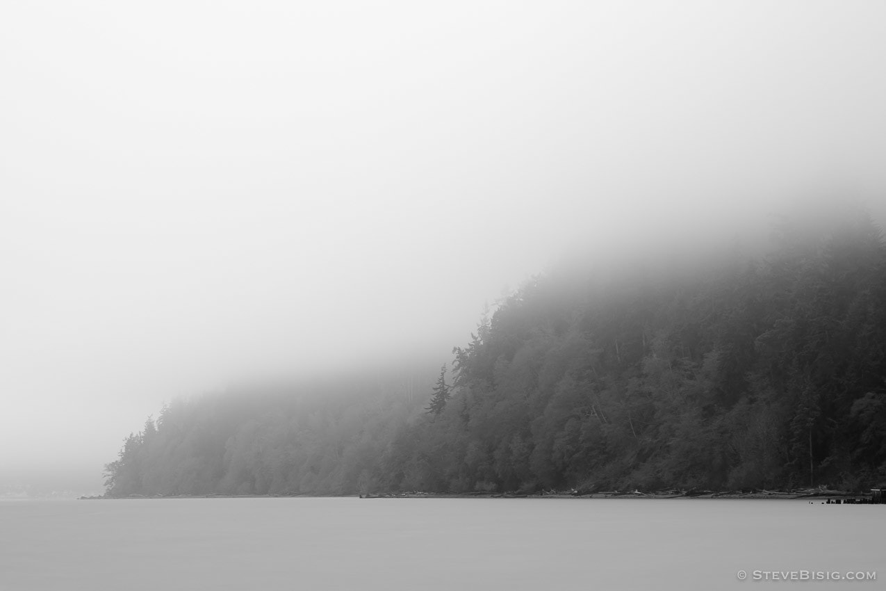 A black and white long exposure photograph of the misty shoreline near Ala Spit on Whidbey Island, Washington.