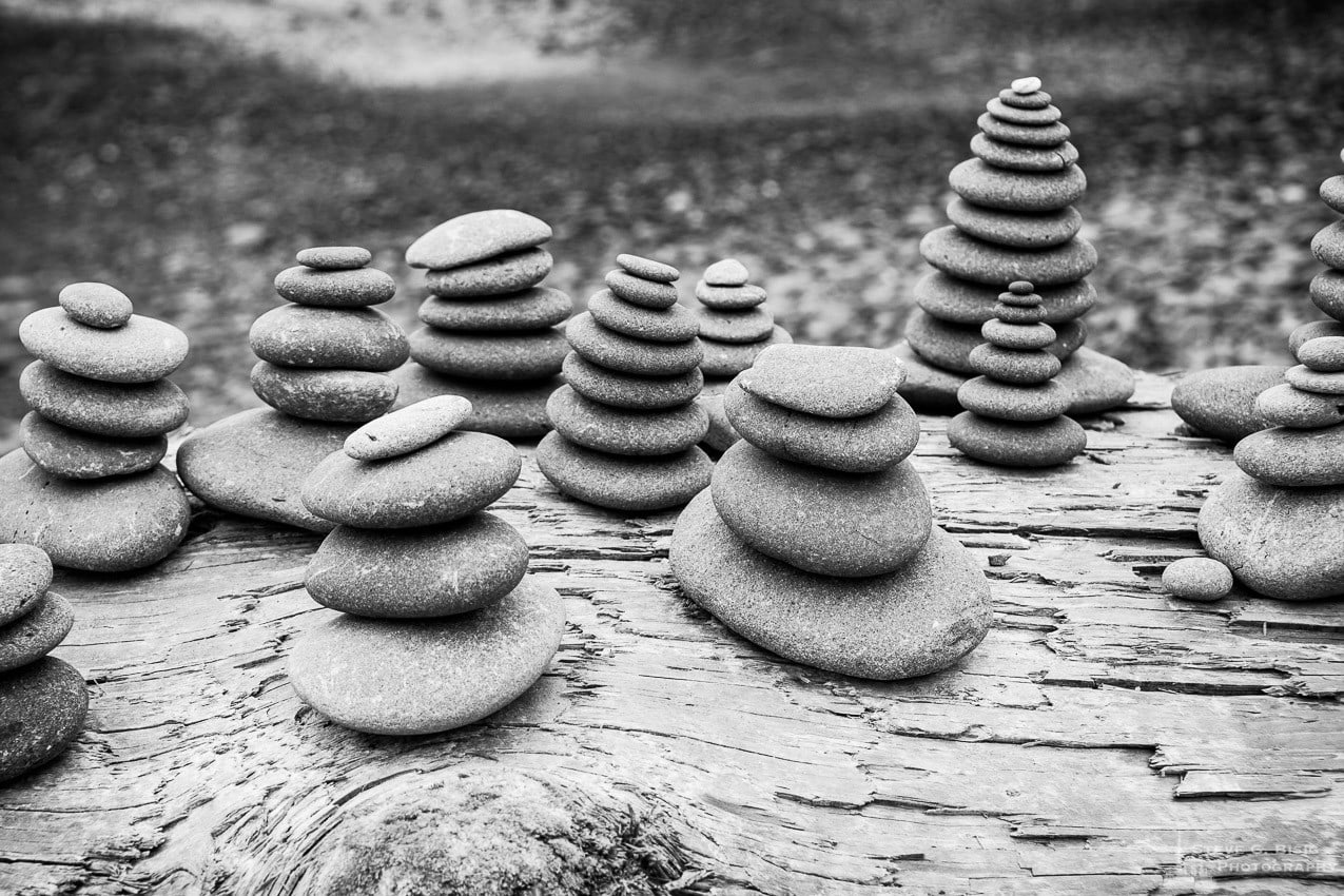 A black and white photograph of a group of rock cairns stacked on a driftwood log at Ruby Beach in the Olympic National Park in Washington State.