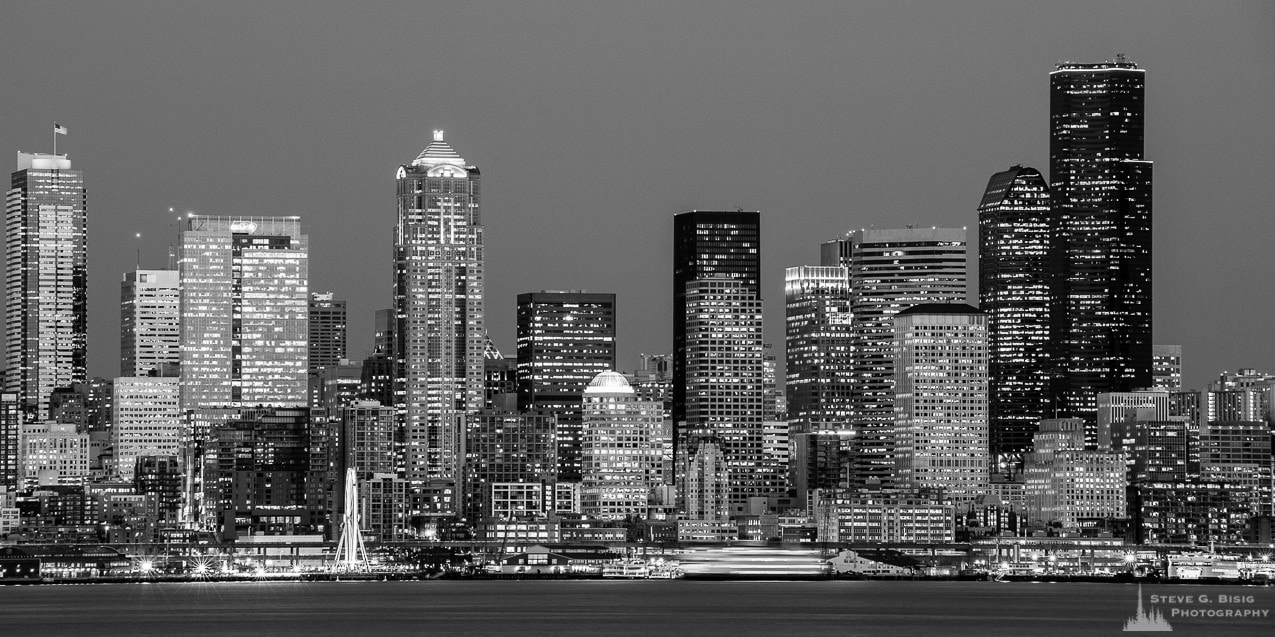 A black and white panoramic photograph of downtown Seattle, Washington skyline over Elliott Bay on a late Winter night.