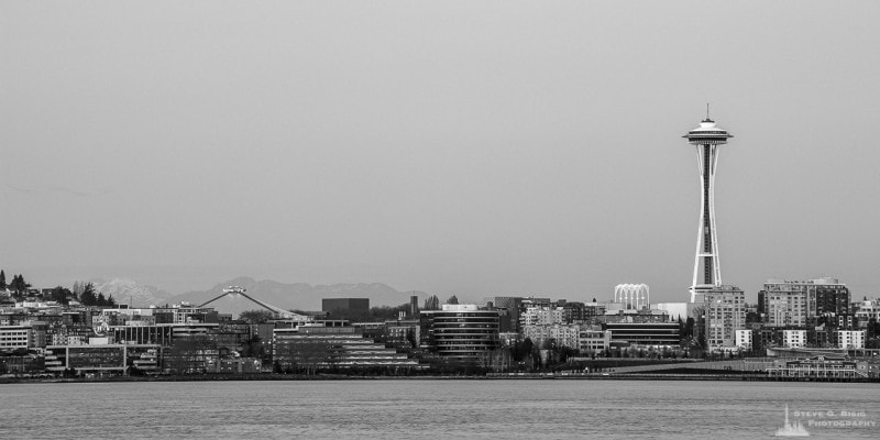 A black and white panoramic photograph of the Space Needle and the Seattle, Washington skyline over Elliott Bay as seen from Alki Point just before dusk on a late Winter evening.