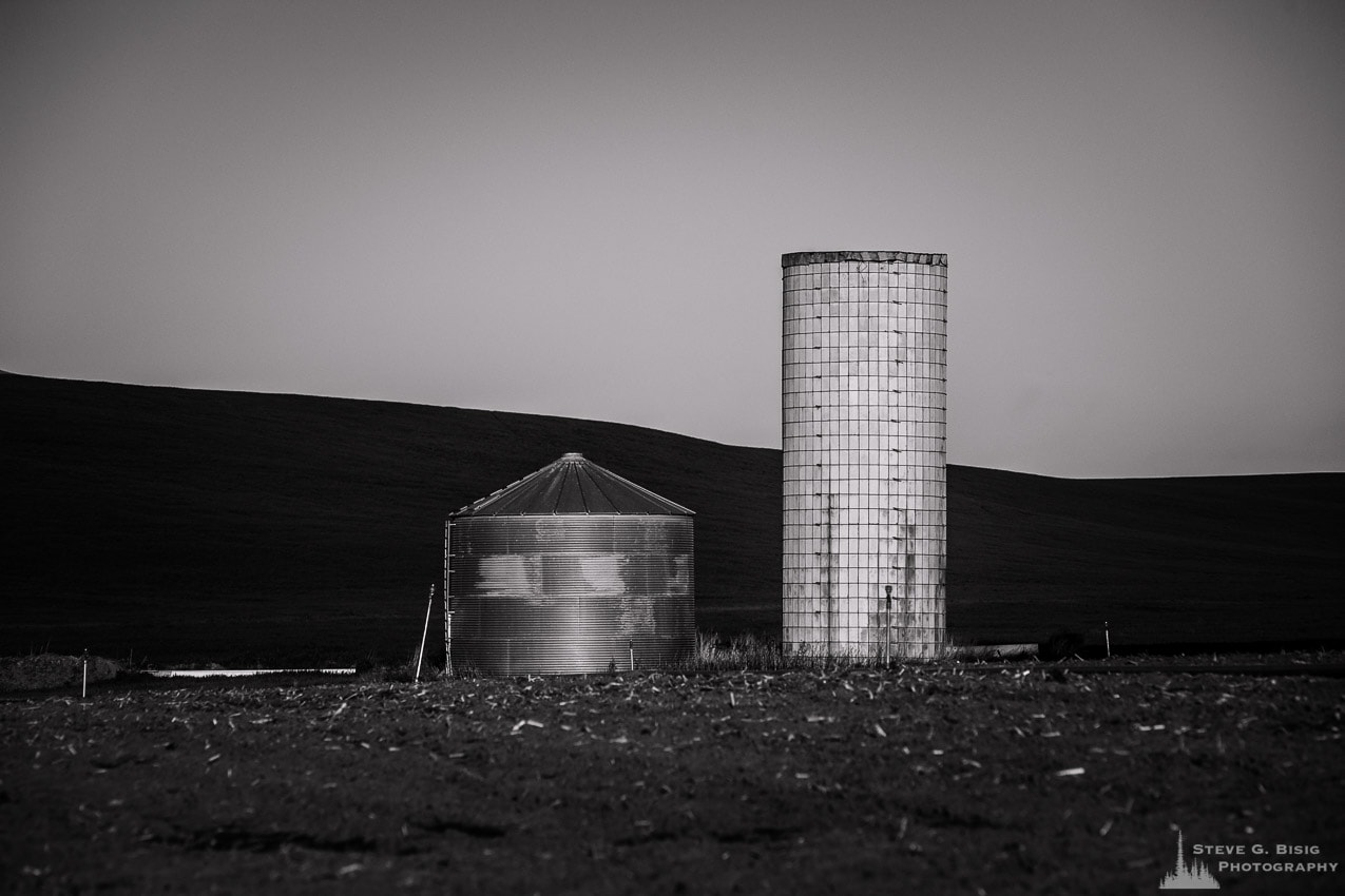 A black and white photograph of an old and a new grain silo standing next to each other in rural Kittitas County near Ellensburg, Washington.