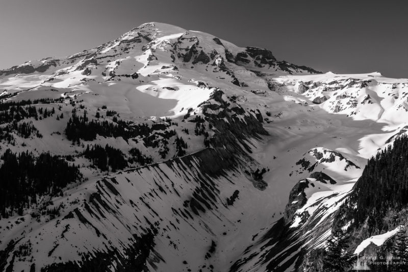 A black and white landscape photograph of Mount Rainier with the last light of a sunny Spring day shining on it as viewed from the Nisqually Vista in the Paradise area of Mount Rainier National Park, Washington.