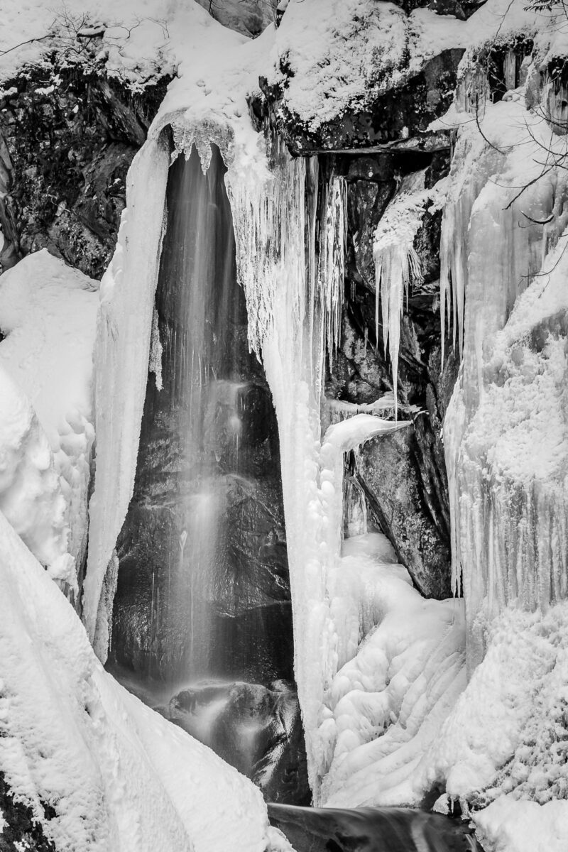 A black and white nature photograph of a snow covered, partially fozen Christine Falls at Mount Rainier National Park, Washington.