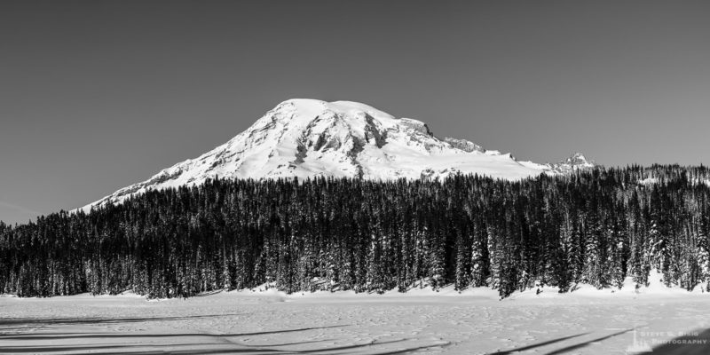 A panoramic black and white landscape photograph of a snow covered Reflection Lake below Mount Rainier along the Stevens Canyon Road at Mount Rainier National Park, Washington.