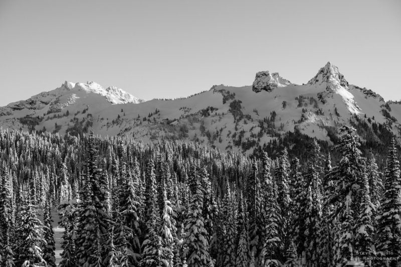 A black and white landscape photograph of a snow-covered Tatoosh Range (Pinnacle Peak, The Castle and Unicorn Peak) captured on a sunny winter day in the Paradise area of Mount Rainier National Park, Washington.