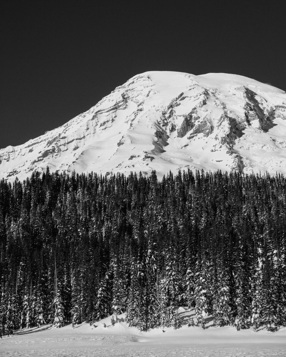 A black and white landscape photograph of Mount Rainier as viewed from a snow covered Reflection Lake at Mount Rainier National Park, Washington.