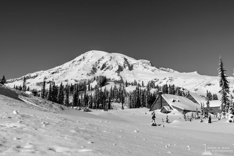 A black and white landscape photograph of Mount Rainier and the historic buildings at Paradise captured on a sunny winter day at Mount Rainier National Park, Washington.