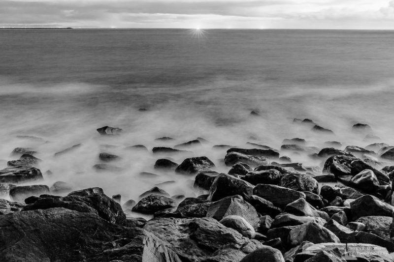 A black and white landscape photograph of the Pacific Ocean at the North Jetty of Grays Harbor at Ocean Shores, Washington on a cloudy winter night.