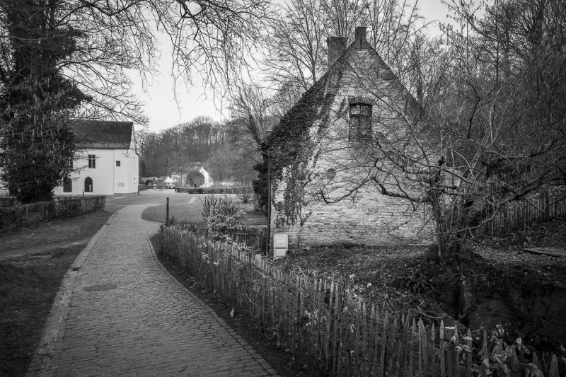 A black and white photograph of the pathway leading past the Miller's House at the Abbaye du Rouge Cloître in Auderghem, Belgium.