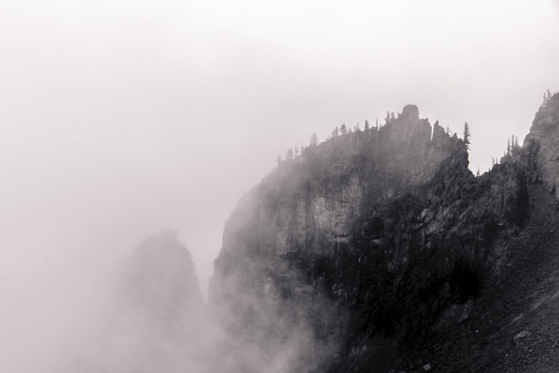 A black and white landscape photograph of rock formations as seen from the Sourdough Ridge trail on a foggy, late Summer day during a visit to the Sunrise area of Mount Rainier National Park, Washington.