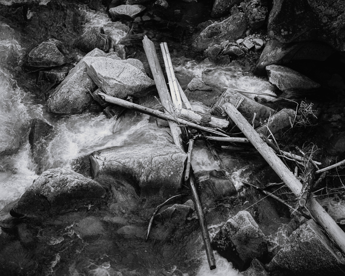 This black and white photograph reveals the untamed spirit of the Entiat River as it surges through Box Canyon, Washington. The contrast highlights the rugged terrain, where the river's powerful current carries through ancient rock formations. Fallen trees, bleached by time, lie scattered along the banks, adding a touch of melancholy to the scene. The interplay of light and shadow creates a sense of depth and mystery, inviting the viewer to explore the hidden corners of this wild and awe-inspiring landscape.