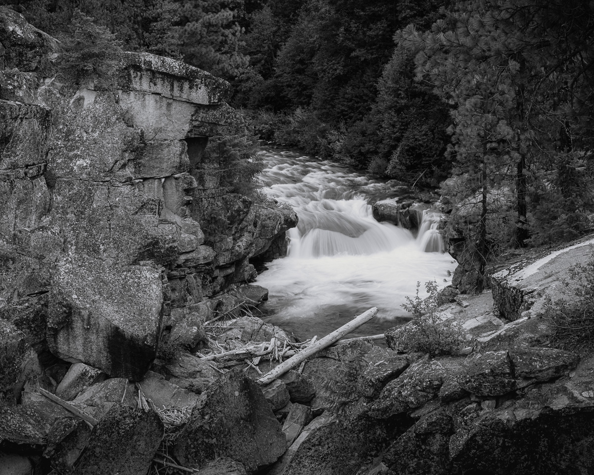 The Entiat River carves its relentless path through the ancient rock of Box Canyon, creating a symphony of rushing water and unyielding stone. This black-and-white image captures the raw power of nature, where millions of years of geological forces meet the ceaseless flow of the river. The stark contrast between the smooth, fluid motion of the water and the jagged, immovable rock formations tells a story of time, persistence, and the ever-changing yet eternal character of our natural world. Here, in this secluded corner of Washington, the primordial voice of the Earth echoes through the canyon, reminding us of the enduring strength and beauty of the untamed wilderness.