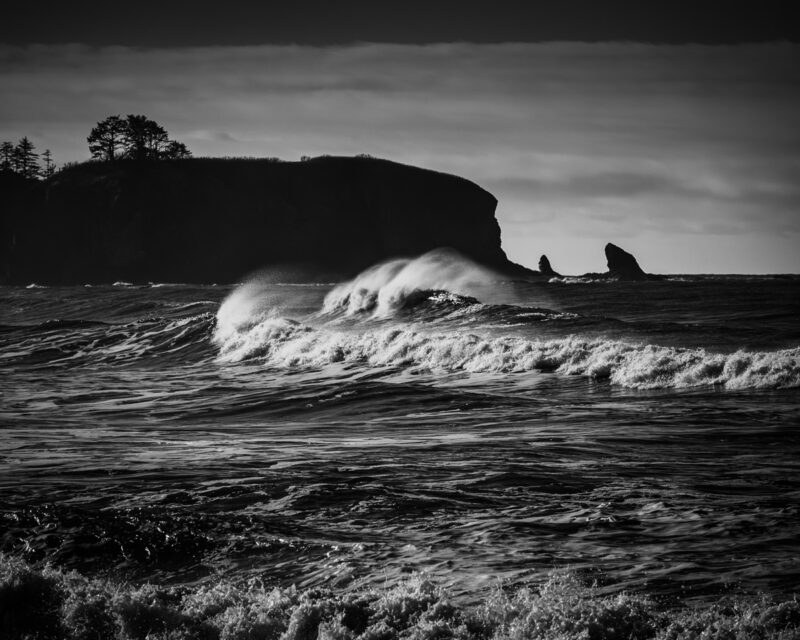 Experience the raw power and serene beauty of Rialto Beach in this black-and-white photograph. The dramatic waves crash against the rugged coastline, capturing a moment of nature's symphony.