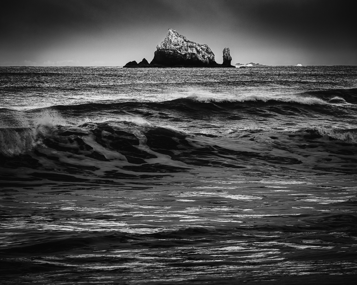 Experience the raw power and serene beauty of Washington's Rialto Beach in this captivating black-and-white photograph. The stormy waves and distant sea stacks evoke a sense of tranquility amidst nature's untamed elements.