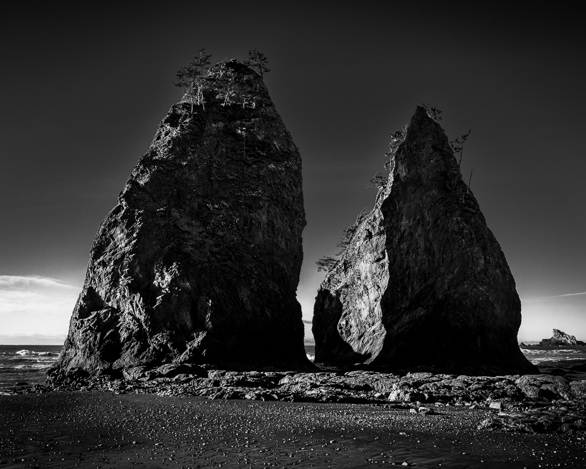 In this black-and-white seascape, the towering rock formations of Rialto Beach stand as timeless sentinels against the vast Pacific Ocean. Their dramatic silhouettes evoke a sense of tranquility and reflection, inviting you to connect with the serene beauty of nature.