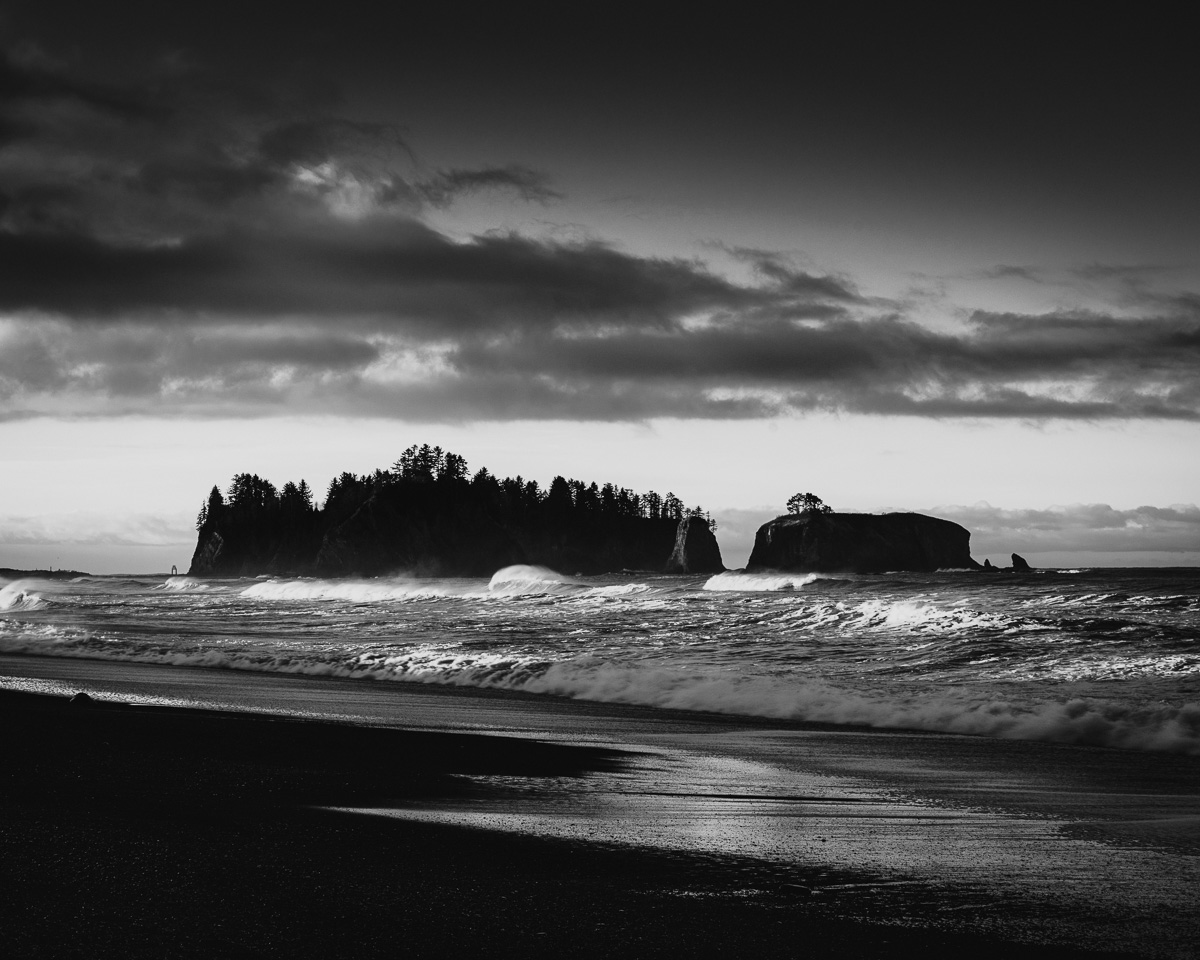 Experience the dramatic interplay of light and shadow at Rialto Beach, where the ocean's timeless dance unfolds in black-and-white elegance. This captivating landscape captures the raw beauty and serene power of the Pacific Northwest's rugged coastline.