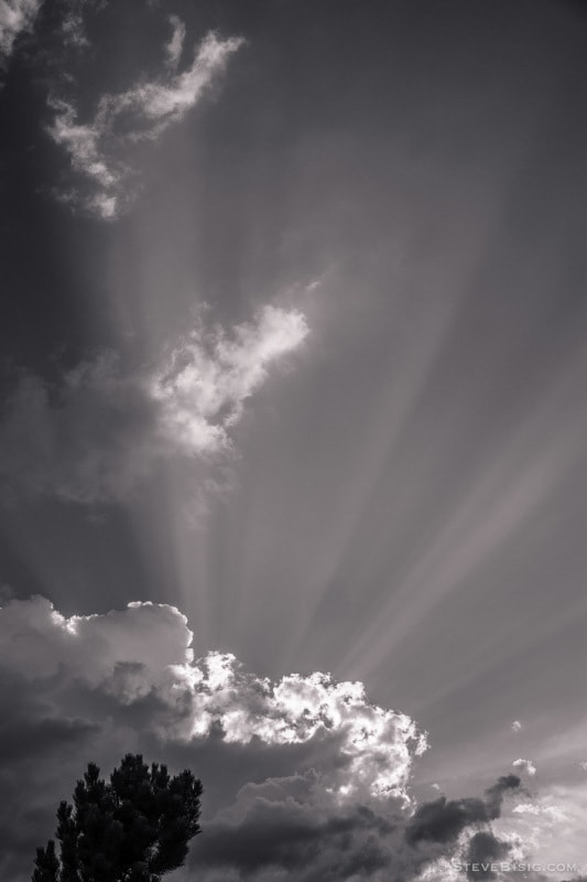 A black and white photograph of a mid-summer thunder storm approaches the Kittitas Valley near Ellensburg, Washington. Rays from the setting sun shine over the dark clouds.