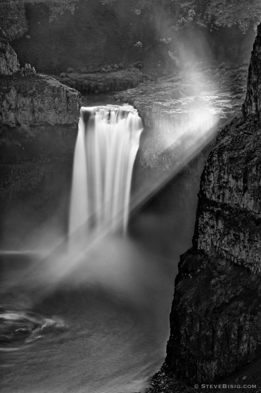 A black and white photograph of Palouse Falls, Washington with Crepuscular rays from the backlit sunlight.