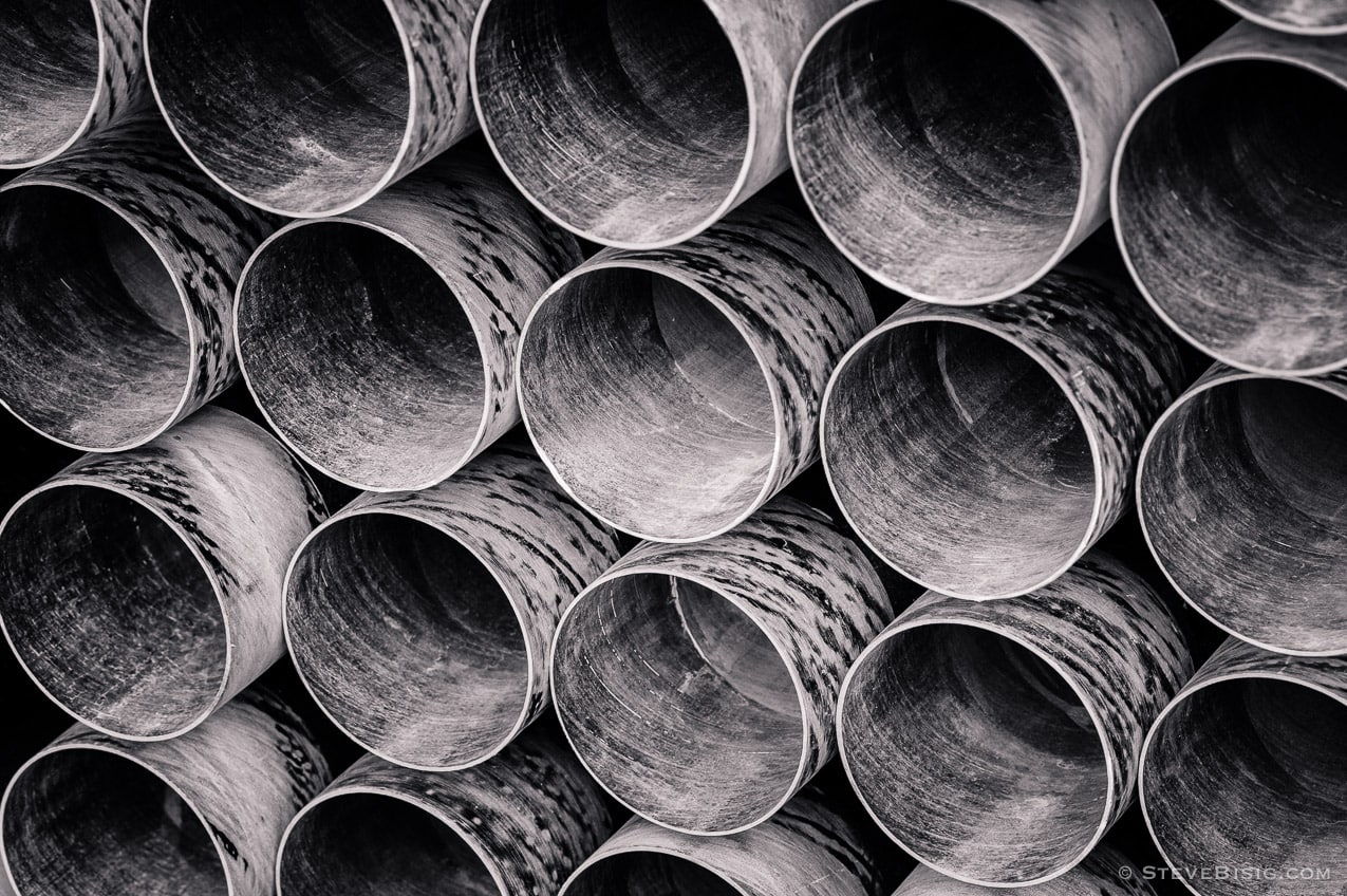 A black and white photograph of a stack of PVC pipes at a construction site in Seattle, Washington. 